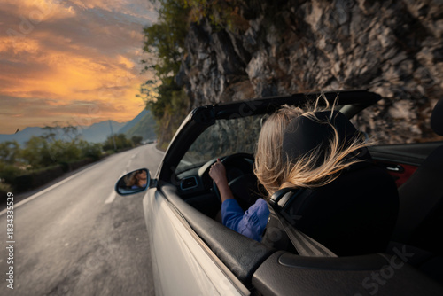 Young woman driving convertible along scenic ocean coast and mountain road at sunset, carefree summer vacation, travel freedom and adventure on coastal highway