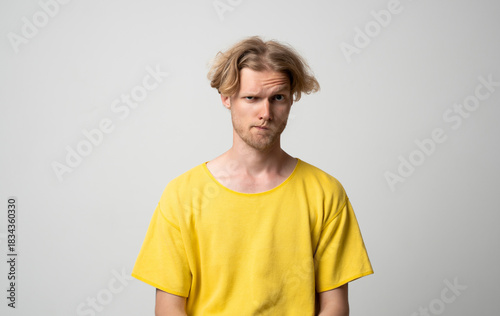 Slika na platnu Skeptical young man in yellow shirt raising eyebrow and looking at camera on lig