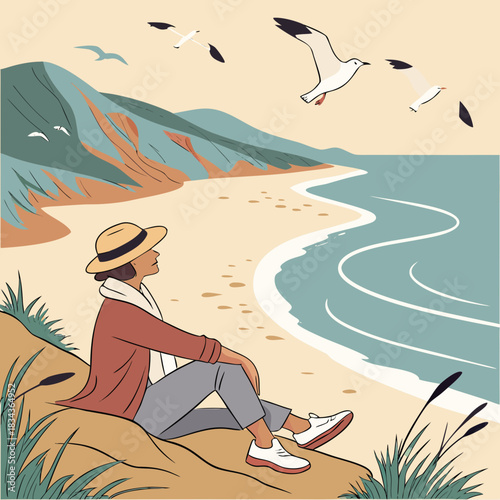 A woman wearing a hat and casual clothes sits on a sandy dune overlooking the ocean and distant hills with seagulls flying above