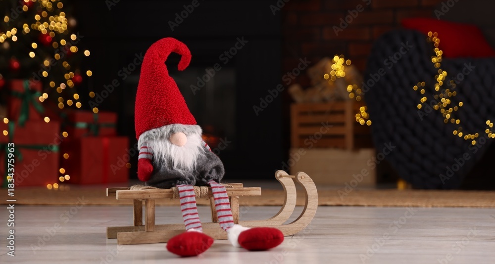 Obraz premium Funny Christmas gnome on wooden sleigh in decorated room. Space for text