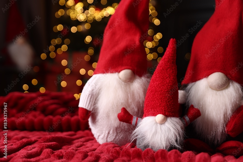 Fototapeta premium Funny Christmas gnomes on red blanket in decorated room, closeup. Space for text