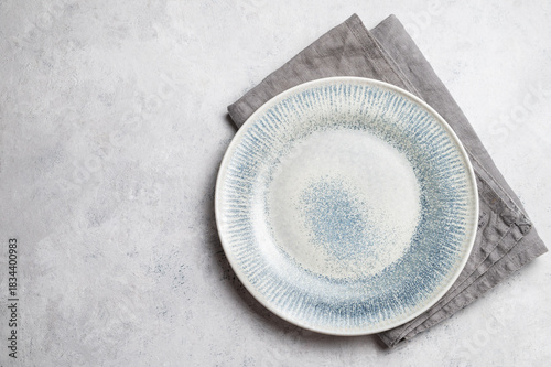 A ceramic blue plate with a linen napkin on a light textured background.
