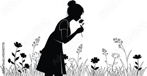 Silhouette of a young girl smelling a flower in a field