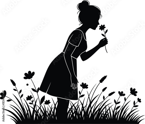 Silhouette of a young woman smelling a flower in a field