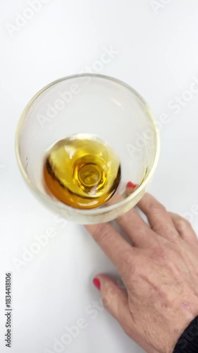 Top View of Mature Hand Swirling Amber Spirit in Glass on White Table