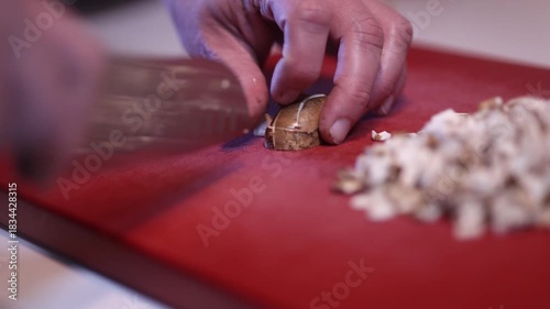 a man's hands cutting mushrooms on a red cutting board in the kitchen