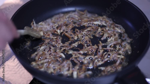 bacon frying in a pan while a man stirs it in his home kitchen