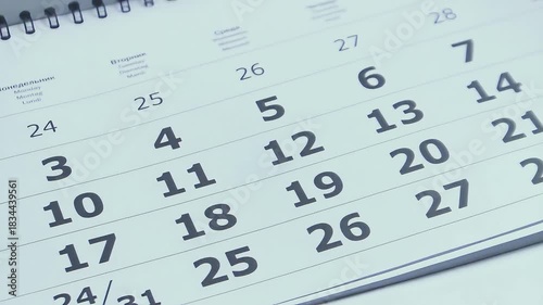 Close up of a white paper calendar as pages rapidly turn upward, dates and months flying by to symbolize the fleeting passage of time, busy schedules and approaching deadlines
