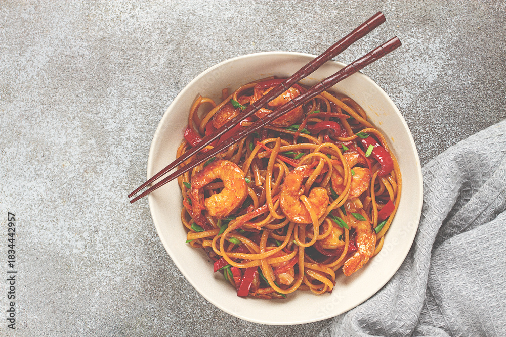Fototapeta premium udon stir-fry shrimp noodles with red bell pepper and green onion, served in a black bowl, with chopsticks, gray background,