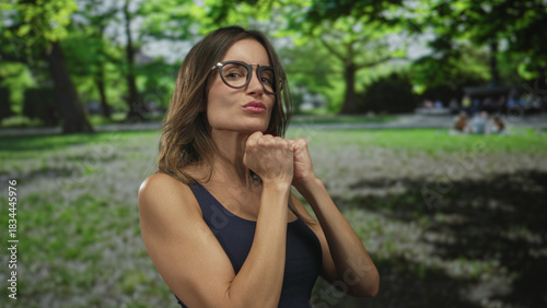 Φωτογραφία Woman wearing black sunglasses and a blue top with clenched fists punching air in park; empowerment