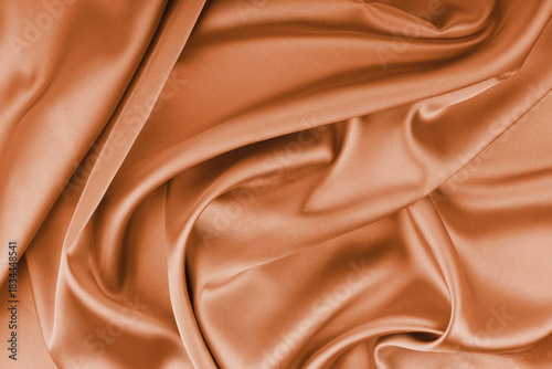 Crumpled, wrinkled orange colored glossy silk satin with wave drapery. Shiny smooth fabric with soft folds, cloth texture . Elegant rich background, wallpaper, backdrop. Flat lay, top view