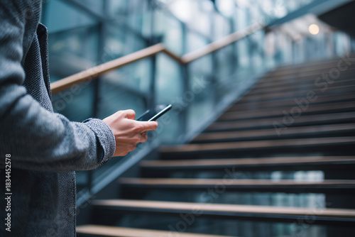 A person is holding a cell phone while standing on a set of stairs