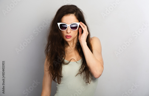 Portrait of elegant woman posing white sunglasses and fashion top on grey wall background with empty copy space for text. Front view face emotion sexy summer studio portrait