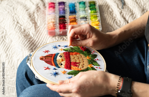 woman stitches an owl design with colorful threads in a cozy indoor setting during daytime