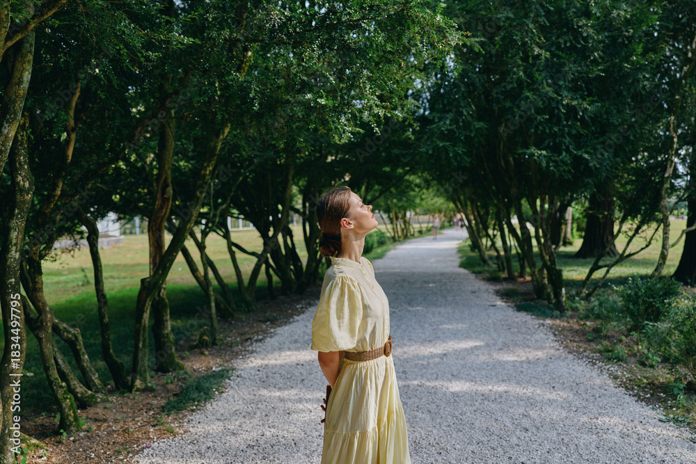 Obraz premium woman outdoors park portrait with yellow dress on a gravel path in a lush environment serene sunlight textures and greenery under trees creating a peaceful summer mood