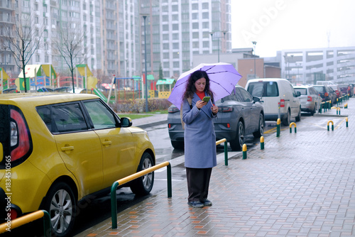 Woman standing outdoors with umbrella and phone