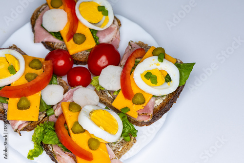Healthy sandwiches made from whole wheat bread with egg, pickles, tomato, and chives arranged on a white plate. The plate with the sandwiches is placed against a white background.