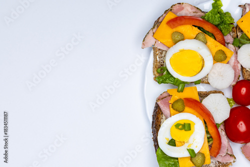 Healthy sandwiches made from whole wheat bread with egg, pickles, tomato, and chives arranged on a white plate. The plate with the sandwiches is placed against a white background.