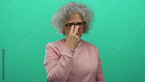 Elderly woman with grey hair gesturing vigilance against a green background, wearing glasses and a pink sweater, adds an intriguing focus to social awareness.