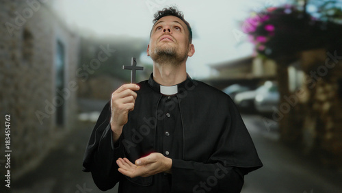 Bilde på lerret Priest holding cross outdoors wearing clerical clothing looking contemplative wh