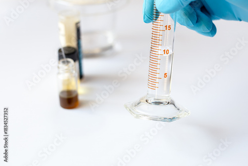 A scientist holds a graduated cylinder containing exactly 10 ml of solvent to prepare the mobile phase for Thin Layer Chromatography (TLC) analysis.
