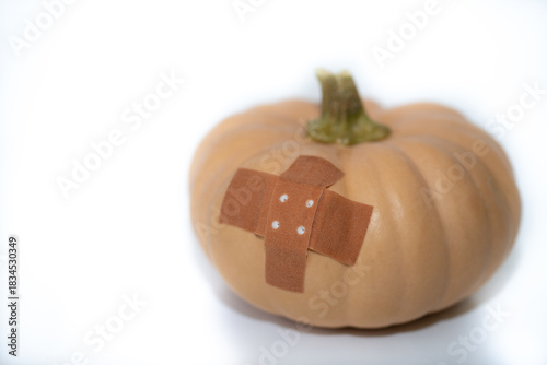 A small brown edible pumpkin stands in front of a white background. There is a brown bandage on the pumpkin. There is space for text.