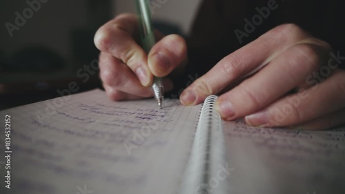 A person writes down notes in a spiral notebook using a pen while sitting in a cozy, softly lit space in the evening hours.