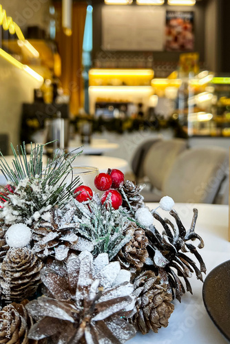 Close-up of Christmas decor on a table in a cozy, warmly lit cafe interior. Blurred background of a coffee shop with a display window. No people. Vertical
