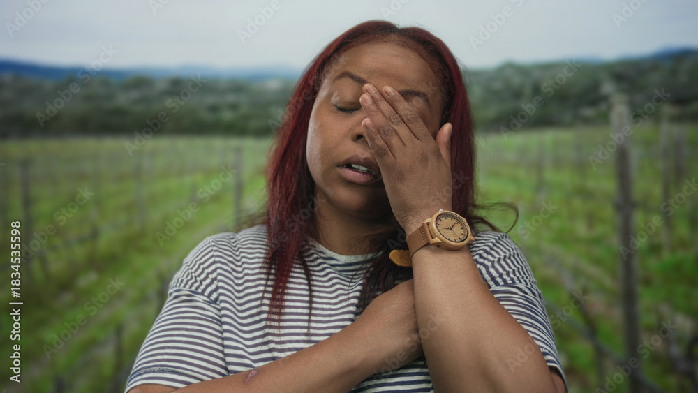 Obraz premium Woman resting head on hand with eyes closed in forest among vineyard stakes wearing striped shirt; exhaustion.