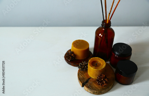Wax bees candles on a wooden candlestick near beauty brown container and fir tree natural cones. Closeup ornament holiday background concept with white empty copy space. Natural day light