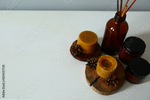 Wax bees candles on a wooden candlestick near beauty brown container and fir tree natural cones. Closeup ornament holiday background concept with white empty copy space. Natural day light