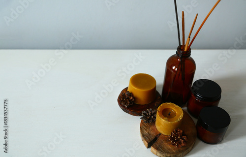 Wax bees candles on a wooden candlestick near beauty brown container and fir tree natural cones. Closeup ornament holiday background concept with white empty copy space. Natural day light