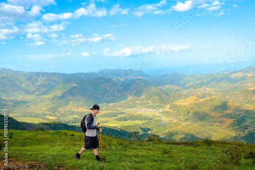 Brazilian man hiking in the mountains while holding a trekking pole.  In the background, a beautiful landscape of green mountains and valleys.