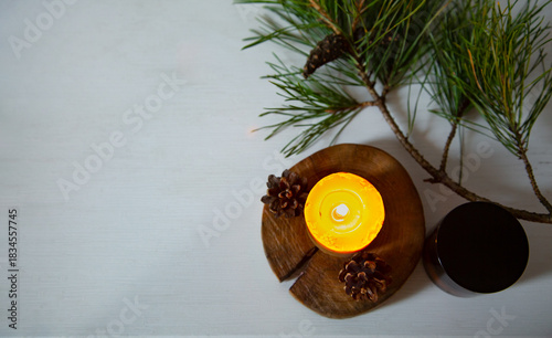 Burning candle fire on a wooden candlestick near green Christmas fir tree branch. Closeup ornament holiday background design concept with white empty copy space. Flat top view. Natural day light