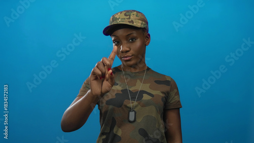 Woman in camouflage uniform wearing dog tags pointing finger up with serious expression in studio; caution.