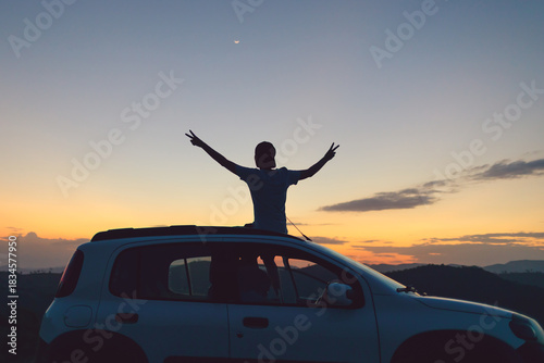Brazilian traveler enjoying a sunset road trip moment, arms raised in freedom and joy. Authentic wellness vibe, outdoor lifestyle, mindful travel and positive energy for modern adventure seekers