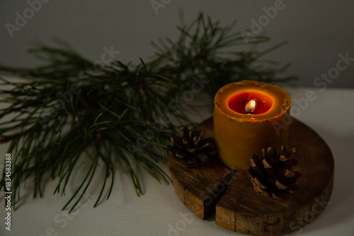 Closeup burning candle fire on a wooden candlestick near green Christmas fir green tree branch. Xmas ornament holiday background concept with empty copy space. Natural day light