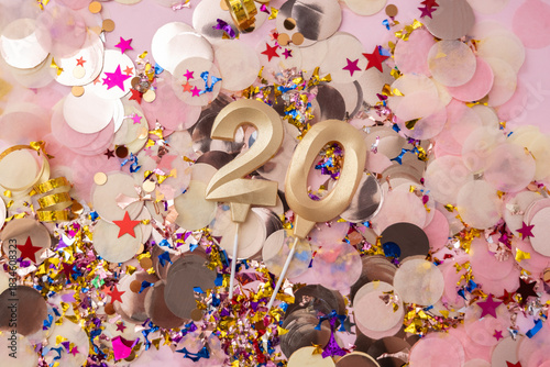 Golden wax candles in the shape of the number 20 on a confetti background. Happy birthday concept. Selective focus