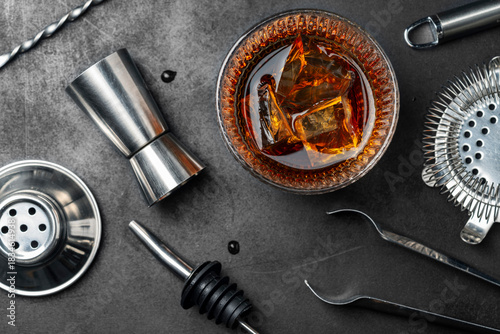 glass of whiskey on the rocks placed among professional bar tools on a dark tbackground