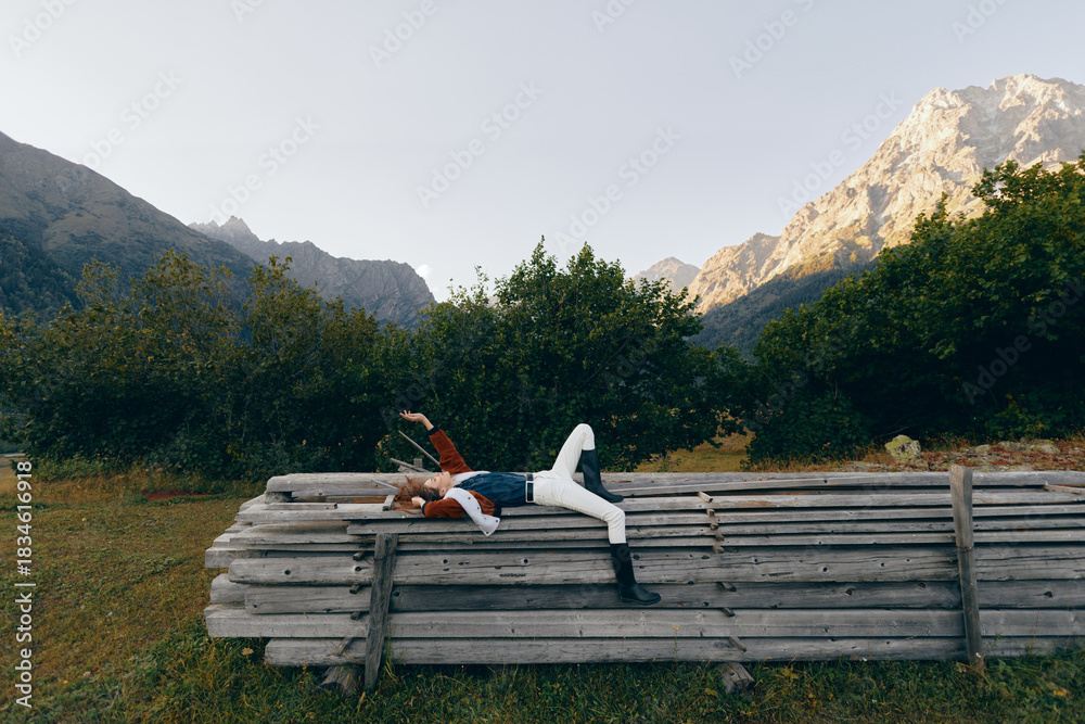 Fototapeta premium Person woman lying on logs in meadow, mountains and forest background, nature relaxation and outdoors resting pose during travel or escape, peaceful countryside scene with greenery