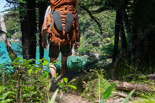 Hiker with backpack and flip flops on coastal forest trail, Abel Tasman, NZ