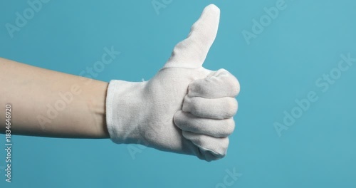 Woman in cloth glove showing thumbs up on light blue background, closeup