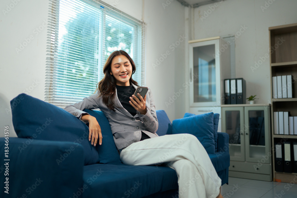 Obraz premium Asian businesswoman relaxing on sofa using smartphone