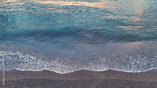 Cinematic slow motion style waves on beach drone footage for relaxation projects featuring the gentle movement of the sea over smooth pebbles during a beautiful summer evening
