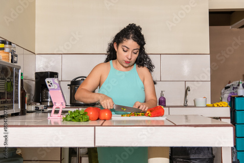 Young Hispanic woman preparing food while filming herself in kitchen