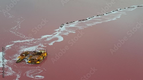 Close-up aerial view of a yellow salt dredging platform operating on the pink waters of Laguna Salada de Torrevieja, Spain, during mineral extraction.