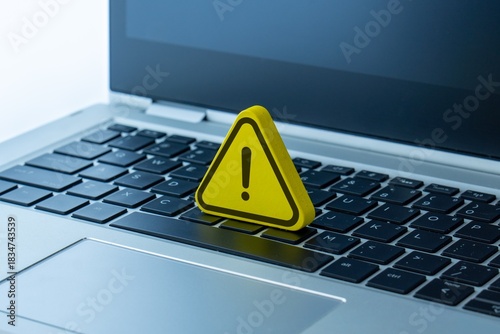 A yellow warning sign with an exclamation mark placed on a laptop. Cybersecurity, computer error, system alert, online danger concept.