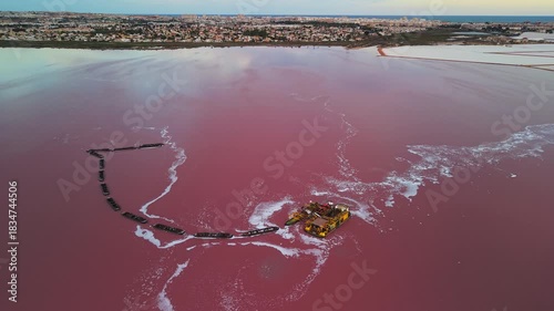 Aerial view of salt mining barges on a pink lake near Torrevieja. The floating platforms and tugboats are extracting salt from the vividly colored water