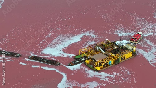 Industrial salt harvesting barges working on the vivid pink waters of a salt lake near Torrevieja, Spain, viewed from above during the extraction process.