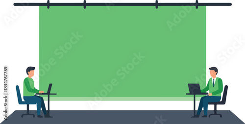 Two people seated at desks with laptops before a large green screen setup